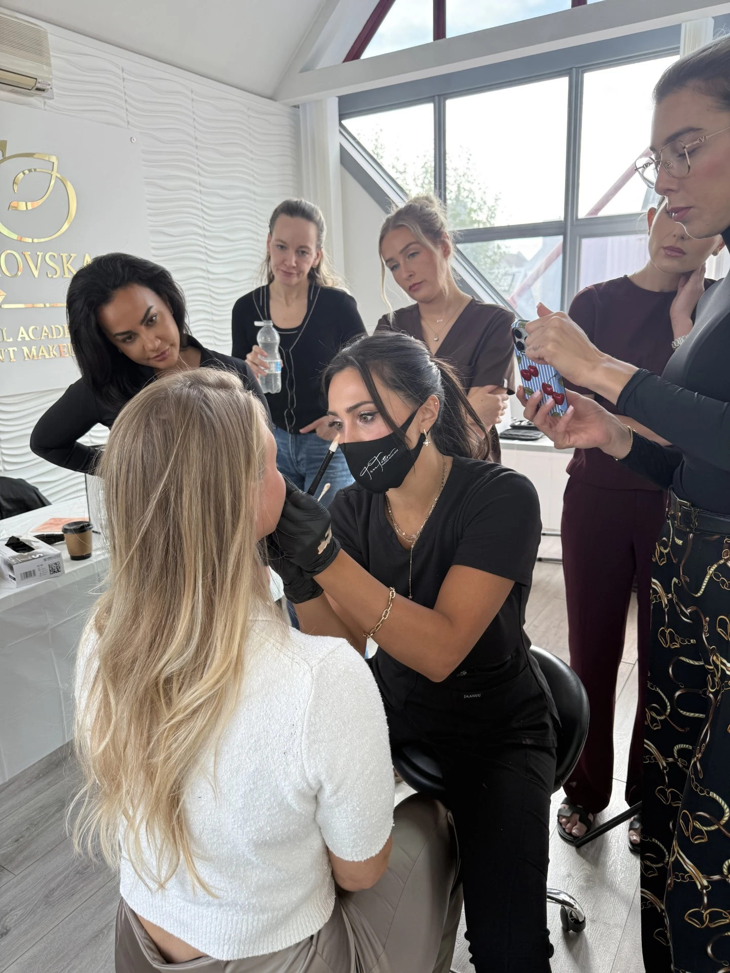 Artist performing a brow treatment on a client while students observe during training